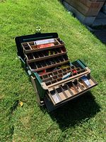 Open tackle box showing multiple trays filled with fishing tackle such as lures, hooks, and other items.