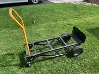 Side view of HARPER heavy duty dolly with yellow handle, black metal frame, large rear wheels and smaller front caster wheels on grass.