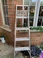 Full view of the 5-rung folding metal ladder showing paint splatters and wear marks.