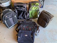 All seven luggage pieces arranged on the floor showing variety of brands and colors including black, green, and brown.