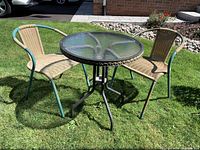 Full view of outdoor bistro set including round glass-top table and two wicker chairs with turquoise metal frames on lawn.