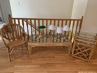 Wicker furniture including an armchair, coffee table with glass top, nested tables, and multiple lamps lined up on the coffee table