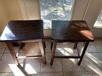 Top-down view of two dark wooden bar stools showing square tops and slight wood grain.