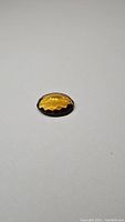 Close up of 14ct deep golden citrine oval cut gemstone on a plain background, showing the faceted surface and deep color.