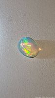 Close-up photo of the 1.88ct Ethiopian opal showing bright green and yellow play of color on a grey background.