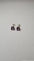Pair of cushion-cut purple amethyst earrings in sterling silver shown from front at slight angle on a white background.