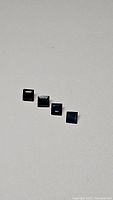 Four square cut blue sapphire gemstones shown in a line, highlighting the deep blue color and various sizes.