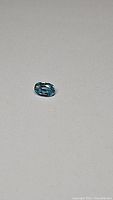 Oval cut lagoon blue zircon gemstone set against a light background showing the stone's color and clarity.
