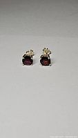 Pair of cherry red garnet stud earrings in sterling silver setting photographed front view showing faceted stones and prong settings.