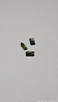 Three emerald cut green sapphire gemstones laid on a white background showing size and color variations including one with blue undertone.