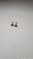 Pair of small square-cut golden citrine stud earrings set in sterling silver shown on plain background.