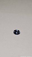 Oval cut natural tanzanite gemstone on plain surface showing deep blue-purple color and brilliant facets under lighting.