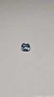 Photo showing a cushion cut blue aquamarine gemstone on a plain light background.