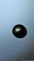 Top view of natural black star sapphire cabochon showing star-like reflection on surface