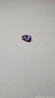 Pear cut natural Brazilian amethyst gemstone on a plain background showing its size, shape and color.