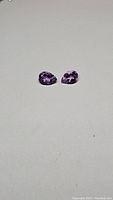 Pair of pear cut purple Bolivian amethyst gemstones side by side on a gray background, showing faceting and clarity.