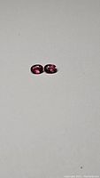 Pair of oval cut purple tourmaline gemstones on white background, showing natural color and size.
