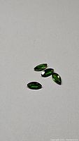 Four marquise cut deep electric green chrome diopside gemstones arranged on a gray surface.