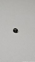 Photo of a round brilliant-cut purple sapphire gemstone with dark intense color and some green undertone on plain background.
