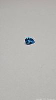 Close-up photo of a pear-shaped blue Swiss Blue Topaz gemstone on a plain surface, showing the vibrant blue color and facets.