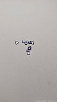 Photo showing nine small pear cut tanzanite gemstones with medium purple-blue color and good clarity scattered on a light gray background.