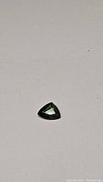 Natural trillion cut forest green sapphire gemstone on plain background, showing shape and color.
