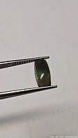 Front and side views of a rectangular cabochon cut untreated black Ethiopian opal held in tweezers, showing its dark body tone and natural green and blue iridescent flashes