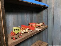 Photo showing a shelf with a variety of cast iron horse-drawn carriages, horses, and toy soldiers in front of a blue wooden panel background.