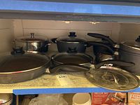 Shelved cookware set with skillets, saucepan, pot, lids, and steamer basket showing condition and included items.