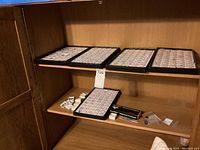 Five black trays on wooden shelf with assorted gemstone holders and a boxed Diamond Analyzer tool