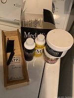 Photo showing wooden box with two gold toothpicks in black sleeves, Medallion brand liquid polish bottles, paste polish tub, and original packaging box.