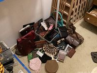 Wide view of assorted handbags and wallets piled on the floor showing a variety of styles including beaded and leather, different colors such as brown, maroon, teal, and black.