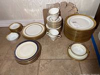 Full view of various stacked porcelain plates and cups, featuring gold accented rims and white bases.