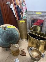 Photo showing metal umbrella stand holding umbrellas and canes, metal platter and magazine holder to the front, rabbit figurine, ceramic pot, and mirror behind the umbrella stand.