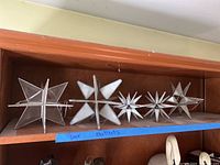 Five Moravian stars on a wood shelf, showing different shapes and glass types including frosted, mirrored, and clear leaded glass.