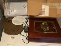 Photo showing the music box wooden case with glass top; energy adapter, instruction disc, and four metal perforated music discs - all placed on a washing machine.