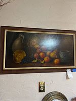 Front view of the framed oil painting showing still life with fruits and pottery, including artist signature.