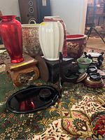Front view showing red and white ceramic vases on wooden stands alongside black ceramic plates and smaller accessories on patterned carpet.
