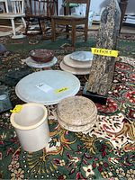 Full lot view showing stone obelisk with dimensions, various marble and stone lazy susans, a crock and bowls on patterned carpet