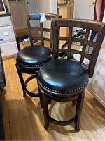 Two wooden kitchen stools with black leather-like seats and nailhead trim, showing overall condition and design.