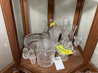 Wide view of twelve clear Waterford crystal pieces including a pitcher, various glasses, bowl, and salt and pepper shakers displayed inside a wooden corner cabinet.