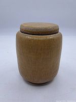 Front view of the ceramic jar with lid on, showing the yellow-brown glaze and smooth texture.