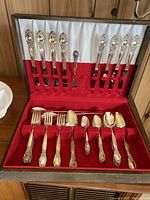 Full flatware set in open wooden case with red velvet and white satin lining, displaying all flatware pieces upright and laid flat.