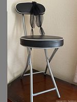 Side and angled view of vintage folding chair showing black cushioned seat and backrest, silver frame, black ribbon tied around backrest