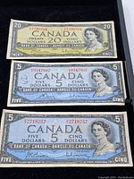 Top-down photo of 3 Canadian banknotes on black background: 1x $20 note, 2x $5 notes, arranged vertically.