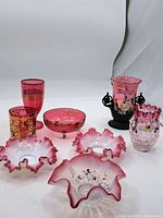 Full view of lot showing cranberry glass dishes, tumblers, and a decorative vase with ruffled edges and gold detailing.