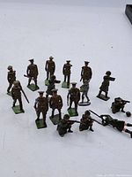 Overview of 15 painted lead soldier figurines arranged on a white surface showing various poses including standing, prone, and kneeling.