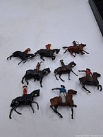 Eight vintage painted lead soldier figurines mounted on horses arranged on white surface showing various military poses and horses in black and brown colors.