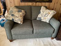 Front view of gray fabric loveseat with two printed leaf-patterned throw pillows on it.