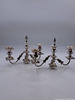 Pair of silver plated 3-arm candle holders side by side with bases not attached, showing overall shape and design.